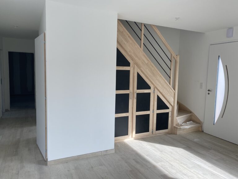 Aménagement d’une entrée de maison avec escalier en bois et rangements sur mesure sous l’escalier.